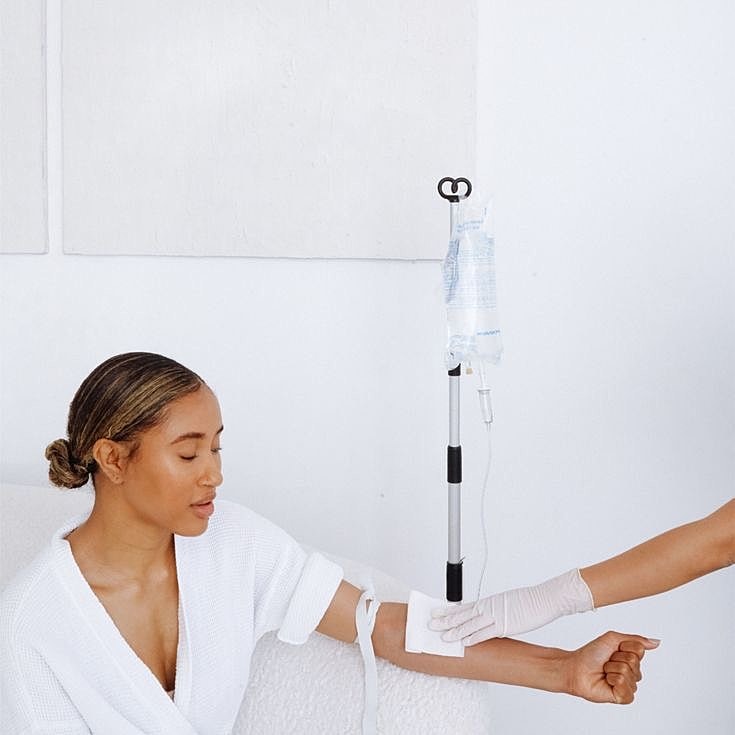 Man receiving IV treatment while smiling and holding water.
